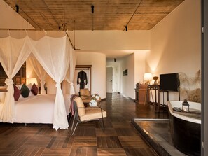 A bedroom with a canopy bed, a sitting area with a chair and table, a TV, and a bathroom with a bathtub. - Anhill Boutique (Hue)