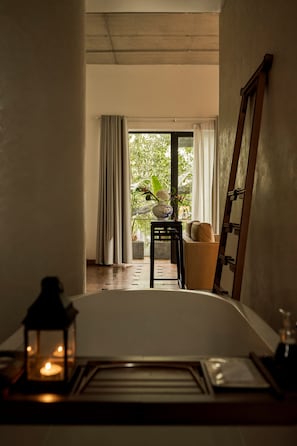 Ein Zimmer mit einem Bett, einem Nachttisch mit Kerze, einer Holzleiter, einem Stuhl, einem Tisch mit Blumenvase und Blick auf Grünfläche.