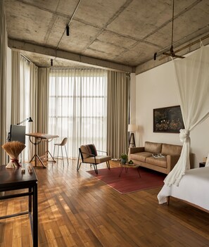 A spacious room with a wooden floor, a bed with a canopy, a sofa, a desk with a lamp, and a chair. - Anhill Boutique (Hue)