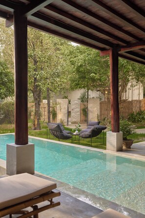 A covered outdoor pool area with lounge chairs and a table, surrounded by greenery and a stone wall. - Anhill Boutique (Hue)