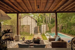 A covered outdoor seating area with a pool, wooden furniture, and potted plants.