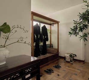 Una stanza con pavimento in legno, uno specchio grande, un comò in legno, una pianta in vaso e una piccola vasetto a forma di elefante.