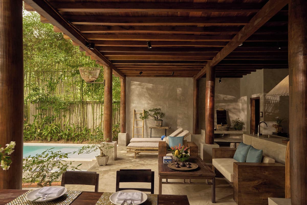 Un espacio al aire libre cubierto con piscina, muebles de madera y plantas en macetas.