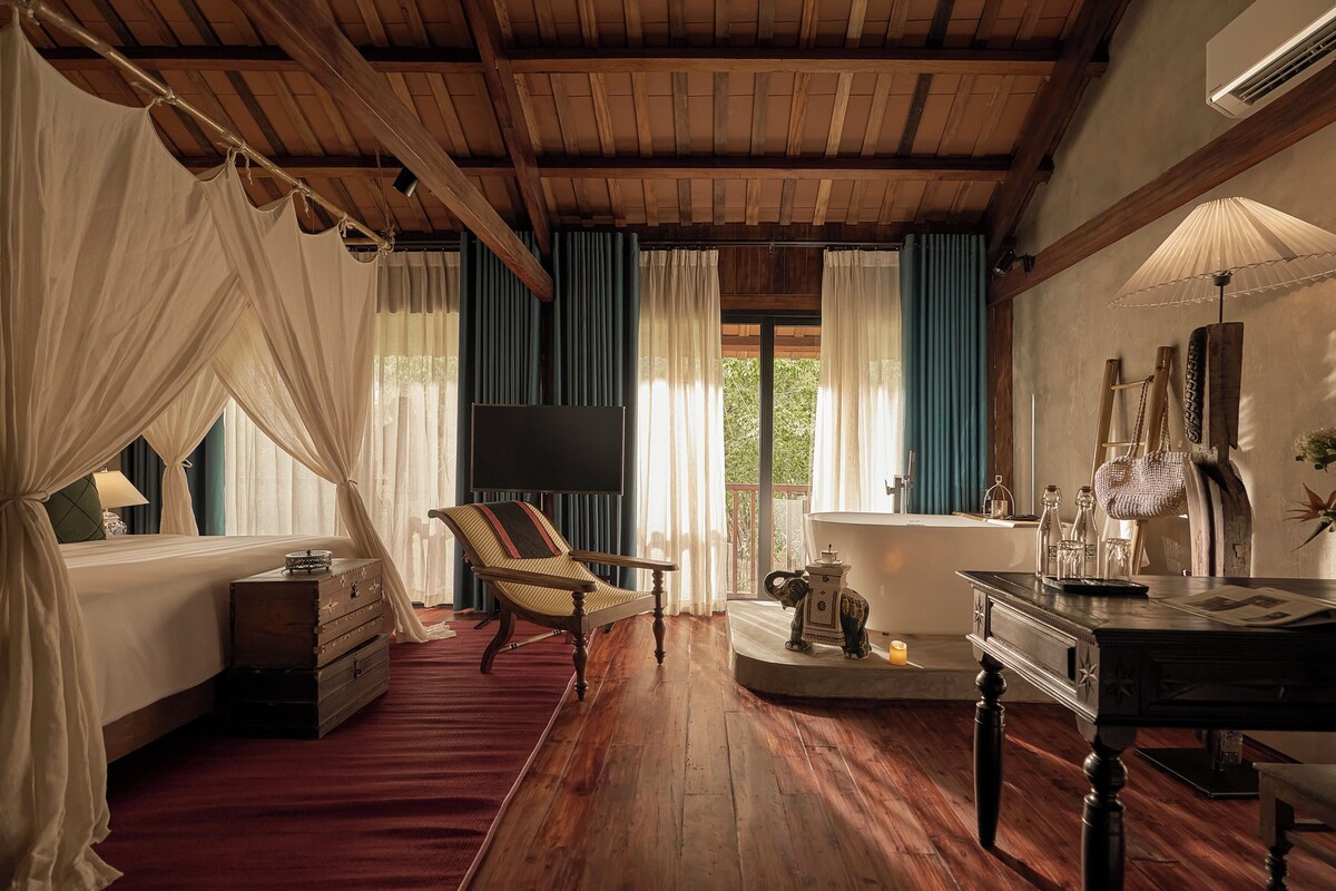 A room with a bed, a chair, a table, a bathtub, and a television.