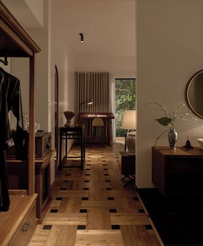 A room with a wooden parquet floor, a desk with a chair, a mirror, a lamp, and a vase with flowers on a side table. - Anhill Boutique (Hue)