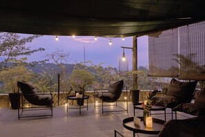 An outdoor seating area with modern chairs and tables, surrounded by potted plants and a view of the landscape. - Anhill Boutique (Hue)