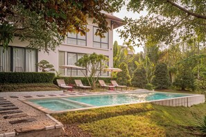 A swimming pool with lounge chairs and umbrellas, surrounded by greenery and a building with large windows. - Anhill Boutique (Hue)