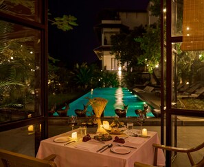 An outdoor dining table set with candles, wine glasses, and plates, overlooking a swimming pool at night. - Anhill Boutique (Hue)