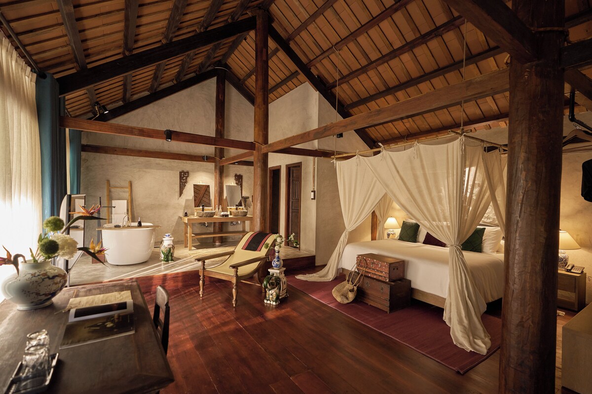 A spacious bedroom with a wooden ceiling, a large bed with a canopy, a bedside table, and a nightstand.