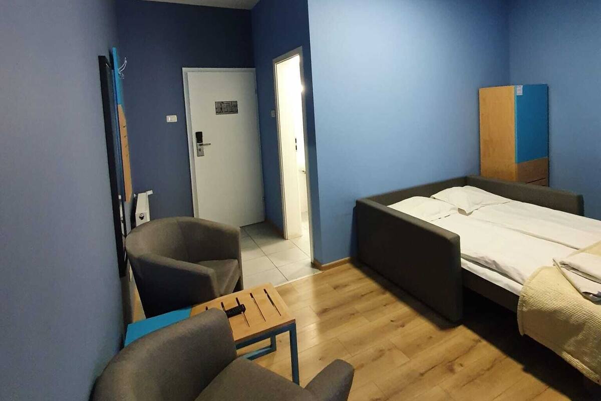Una habitación con paredes azules, una cama, una silla, un escritorio y una puerta.