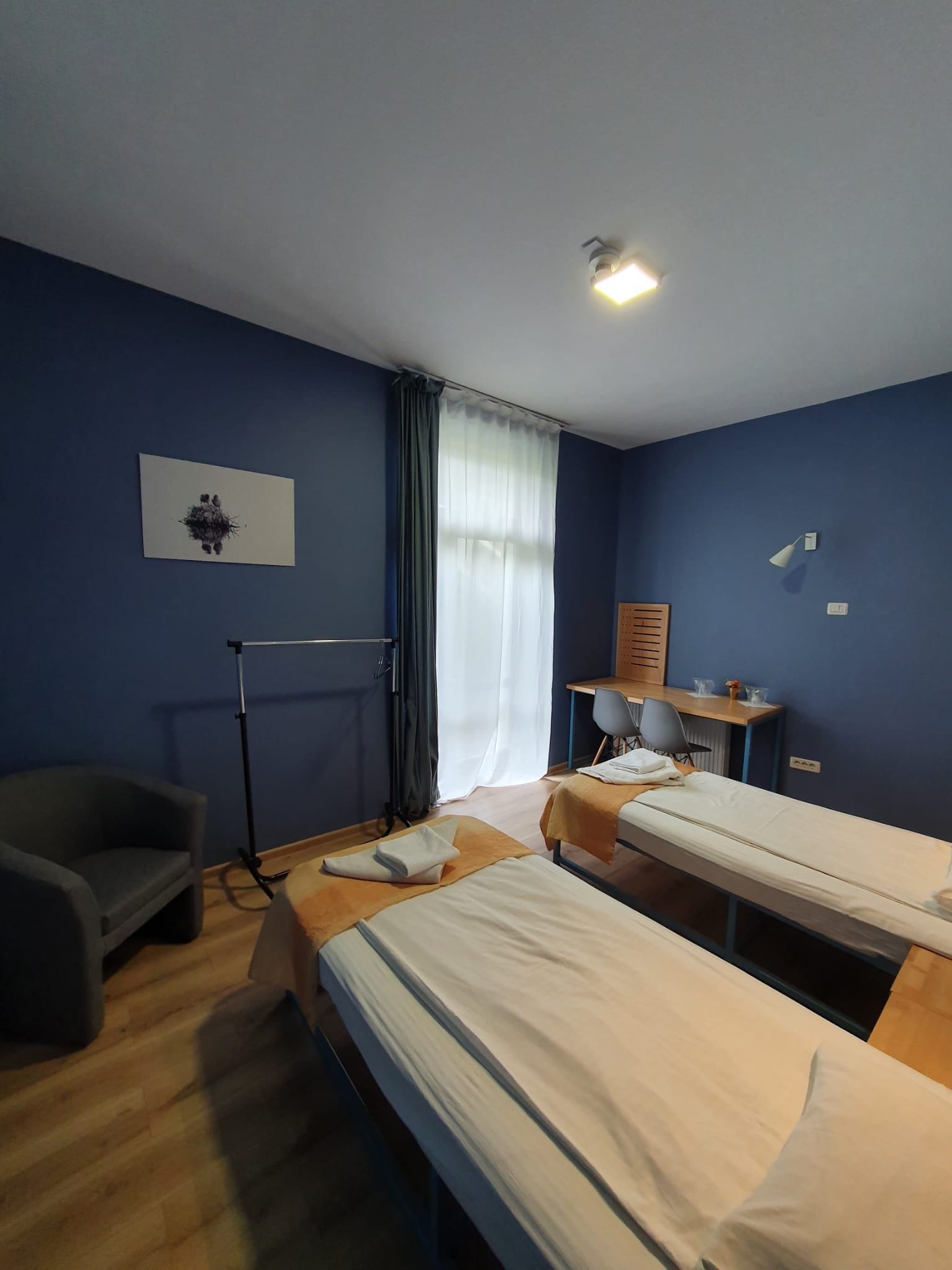 Une chambre d’hôtel avec deux lits, un bureau, une chaise, un radiateur et une fenêtre avec des rideaux.