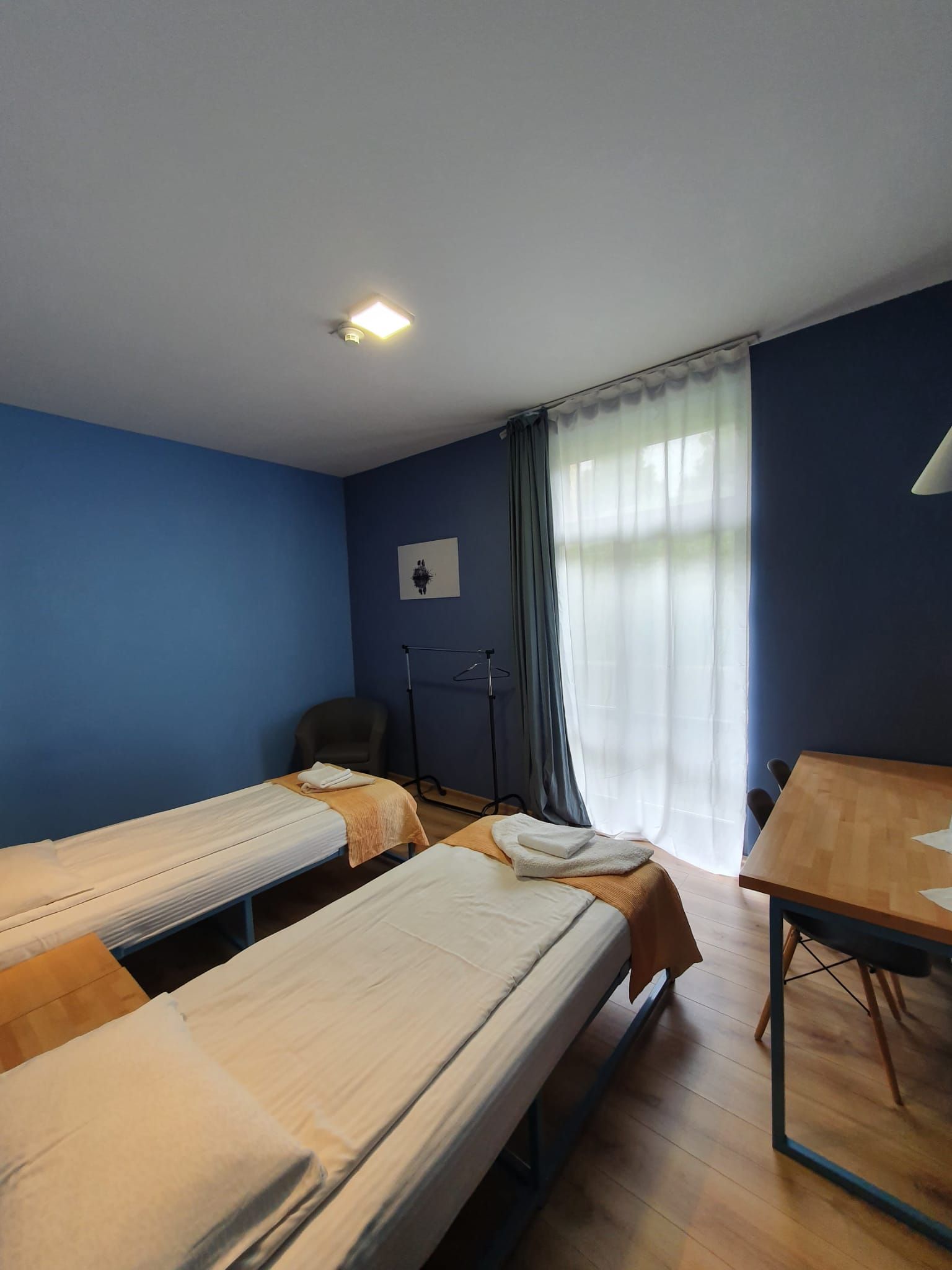 A hotel room with two single beds, a chair, a table, and a window with curtains.