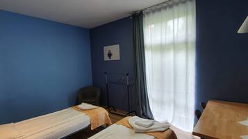 A hotel room with two single beds, a chair, a table, and a window with curtains.