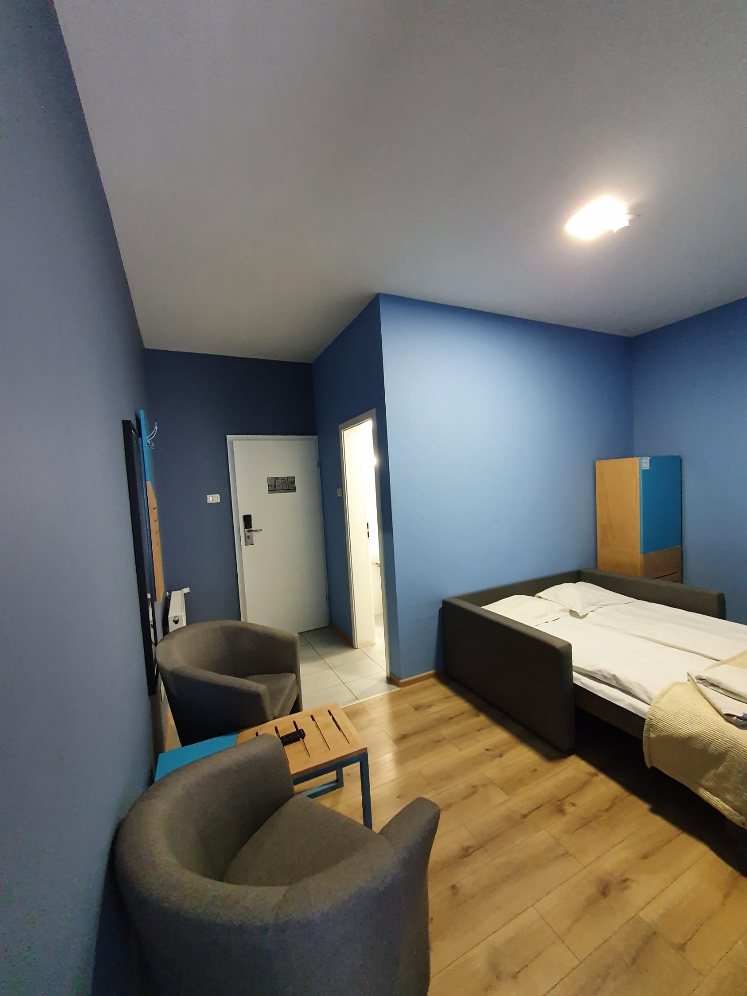 A room with a bed, a chair, a desk, and a door.