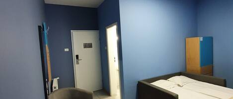 A room with a bed, a chair, a desk, and a door.