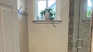 A bathroom with a shower, a towel rack, a window with a plant, and a wooden bench. - Beautiful Farm Style House (Eugene)