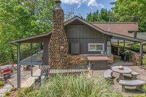 A stone chimney, a covered patio, and a stone table with chairs. - M & M Rockhouse | Pet-Friendly Lake Cottage on Lake Lure with Private Lake Access and Fire Pit (Lake Lure)