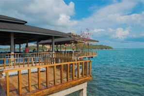A wooden deck with a covered seating area overlooking a body of water, with a view of a distant island. - SBS Resort by Zuzu (Galang)