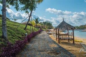 A stone pathway leading to a beach with a thatched-roof structure and a yellow kayak. - SBS Resort by Zuzu (Galang)