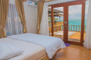 A bedroom with a bed, curtains, and a view of the sea through a sliding door. - SBS Resort by Zuzu (Galang)