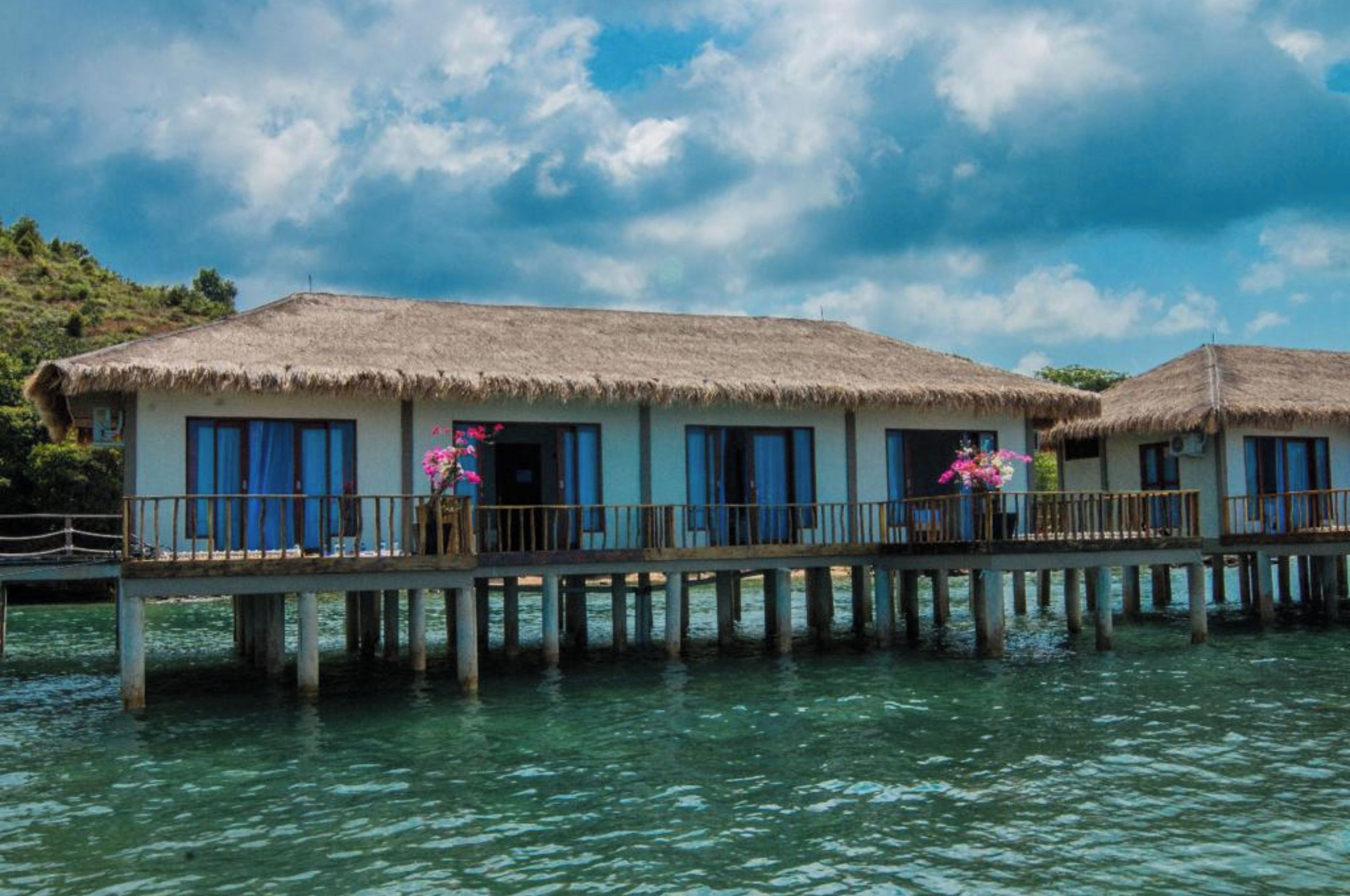 Un bungalow en bord de mer, avec un toit de chaume, une terrasse en bois et une vue sur la mer.