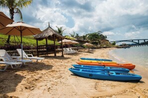 A beach with lounge chairs, thatched umbrellas, and kayaks lined up on the sand. - SBS Resort by Zuzu (Galang)