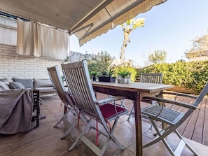 Une terrasse couverte avec une table et des chaises en bois, un canapé et des plantes en pot.