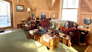 A cozy cabin interior with a wooden ceiling, a sofa with a forest-themed blanket, a lamp, and a deer skull on the wall. - Off grid solar a-frame cabin Northwoods Farm Stay Hundreds of Acres to Explore (Prentice)
