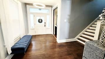 A hallway with a bench, a door with a wreath, and a staircase with a railing.