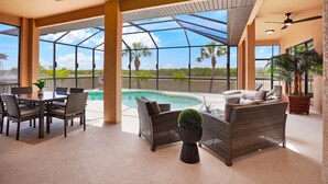 Un espacio exterior techado con piscina, mobiliario de mimbre y ventanas amplias que ofrecen vistas a palmeras.