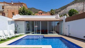 Una piscina con agua cristalina azul, rodeada por un muro blanco y una zona verde.