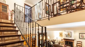 Una escalera con detalles de madera y barandillas negras, que conduce a una sala de estar con chimenea, sofá de cuero y una mesa de comedor.