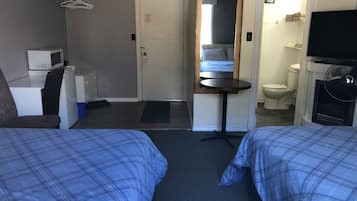 A hotel room with two beds, a desk, a chair, a microwave, a small refrigerator, a mirror, a fan, and a toilet.