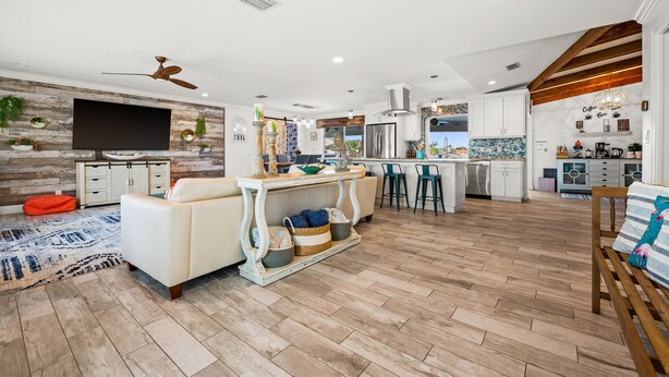 A modern living room with a large TV, a sofa, a coffee table, and a dining area with bar stools. - Beautiful Dog Friendly Home with Screened-in Heated Pool, Game Room/Bar (Cape Coral)