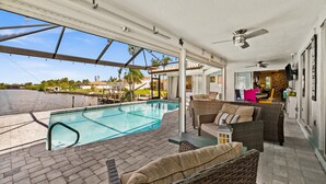 A covered outdoor area with a swimming pool, wicker furniture, and ceiling fans. - Beautiful Dog Friendly Home with Screened-in Heated Pool, Game Room/Bar (Cape Coral)