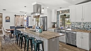 A modern kitchen with white cabinets, a large island with bar stools, stainless steel appliances, and a backsplash with blue and white tiles. - Beautiful Dog Friendly Home with Screened-in Heated Pool, Game Room/Bar (Cape Coral)