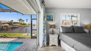 A bedroom with a view of a water body, a bed, a nightstand, and a lamp. - Beautiful Dog Friendly Home with Screened-in Heated Pool, Game Room/Bar (Cape Coral)