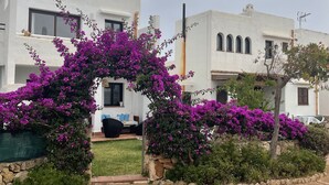 A courtyard with white buildings, a stone pathway, and vibrant purple bougainvillea flowers. - Townhouse, surrounded by gardens and swimming pools (Cala d'Or)