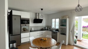 A modern kitchen with white cabinets, a wooden dining table, and a black range hood. - Townhouse, surrounded by gardens and swimming pools (Cala d'Or)