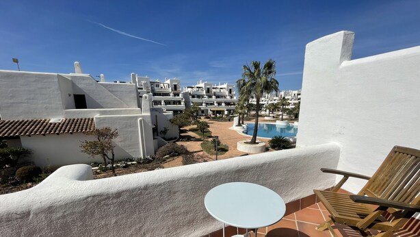 A terrace with a white table and wooden chair, overlooking a pool and white buildings. - Townhouse, surrounded by gardens and swimming pools (Cala d'Or)