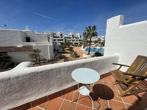 A terrace with a white table and wooden chair, overlooking a pool and white buildings. - Townhouse surrounded by gardens and swimming pools (Cala d'Or)