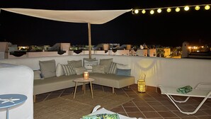 A rooftop terrace with a sofa, a small table, and a chair. There are string lights and a canopy overhead. - Townhouse, surrounded by gardens and swimming pools (Cala d'Or)