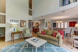 A spacious living room with a high ceiling, a sofa, a coffee table, and a dining area with a table and chairs. - Relaxing, Semi-Private, 2 bed/2 bath, Golf, Beach (Amelia Island)