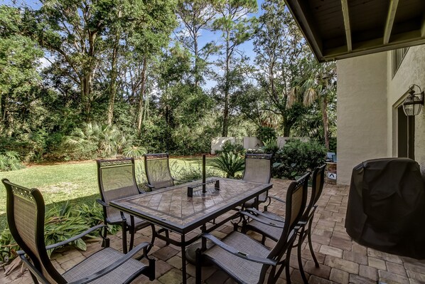 An outdoor patio with a table and chairs, surrounded by lush greenery and trees. - Relaxing, Semi-Private, 2 bed/2 bath, Golf, Beach (Amelia Island)