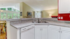 Une cuisine avec des meubles blancs, un plan de travail en granit, un lave-vaisselle et une fenêtre avec des rideaux.