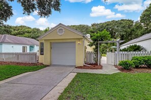 A small, single-story building with a garage door, surrounded by a white picket fence and a well-maintained lawn.