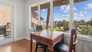 Une pièce avec un bureau et des chaises en bois, de grandes fenêtres donnant sur des palmiers et un terrain de golf.