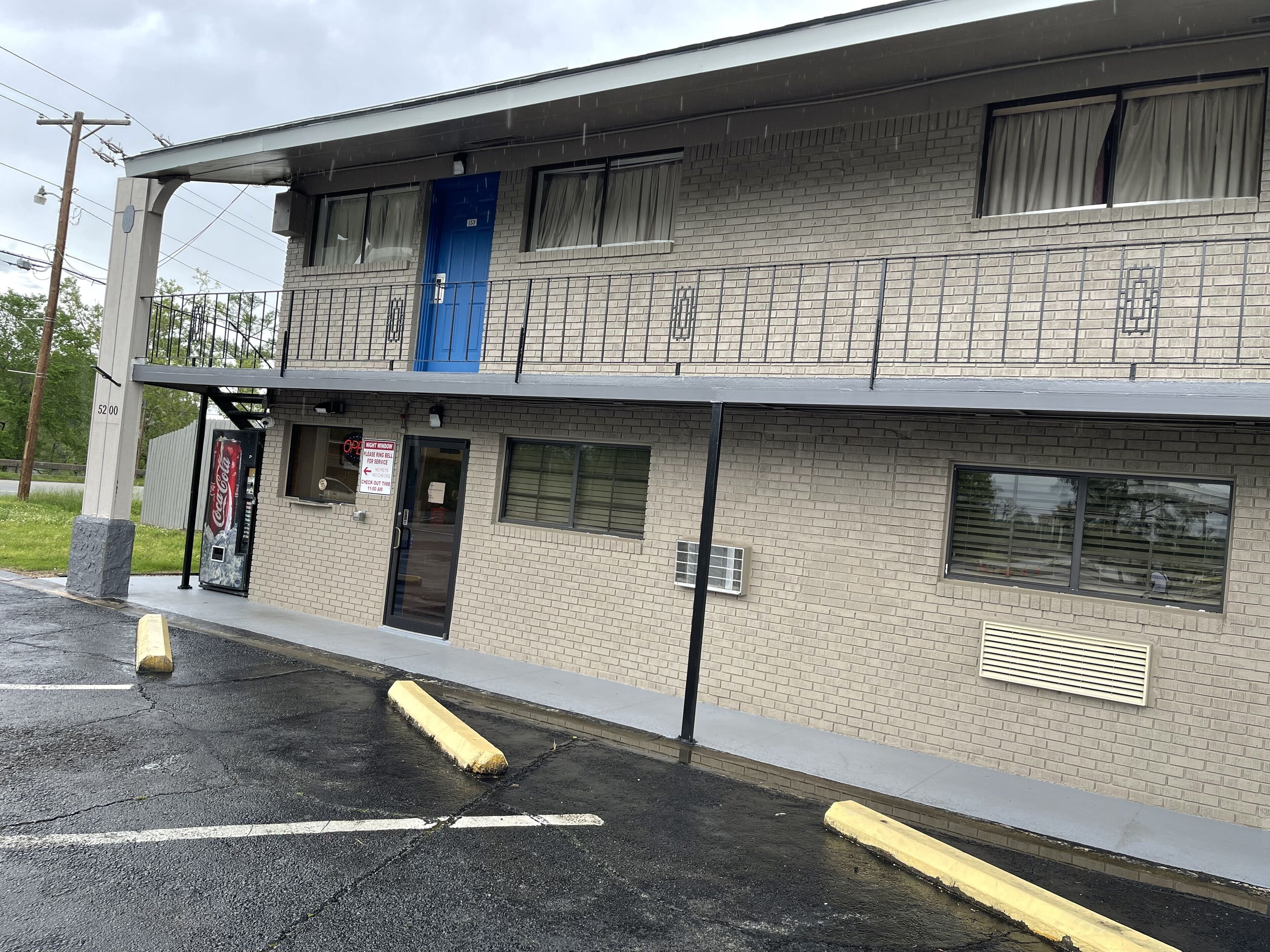 A two-story building with a brick facade, a blue door, and a Coca-Cola vending machine.