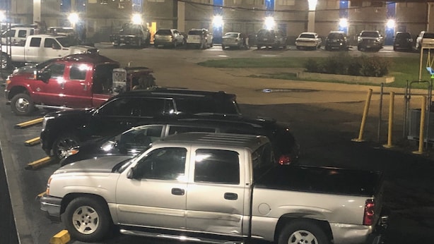 Un estacionamiento con varios vehículos estacionados, incluyendo una camioneta roja y una camioneta blanca.