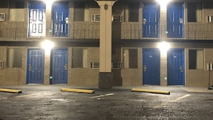 Un edificio de varios pisos con puertas y ventanas azules, una columna central y un estacionamiento con bordillos amarillos.